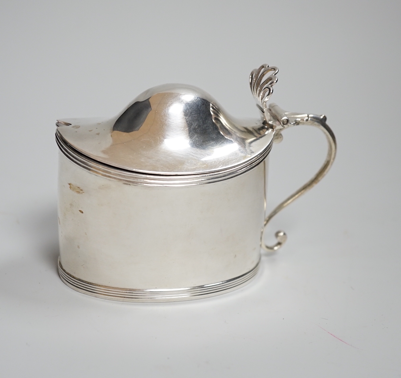 A George III oval silver drum mustard, with domed cover, glass liner and plated spoon, makers Peter, Anne and William Bateman, London 1800, 121 grams